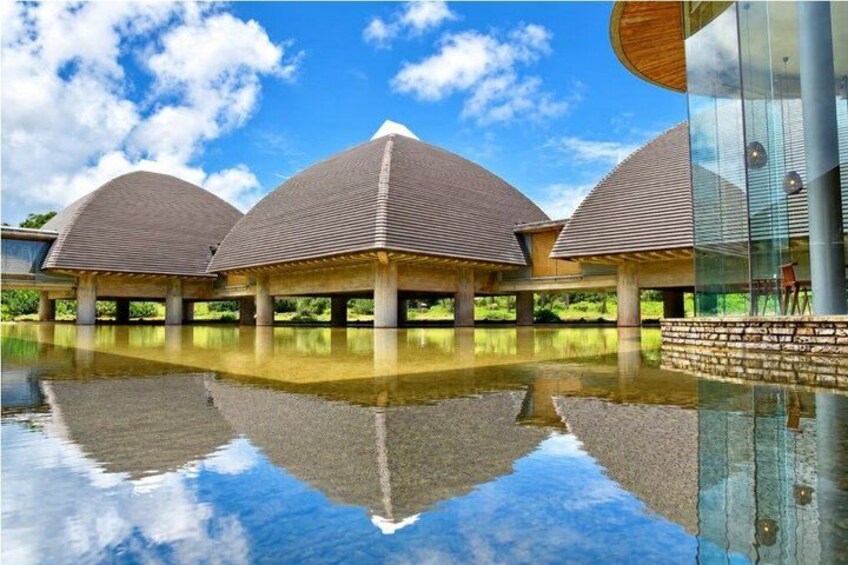 A modern building with three dome-shaped roofs, a reflective water surface, and a clear blue sky. 3