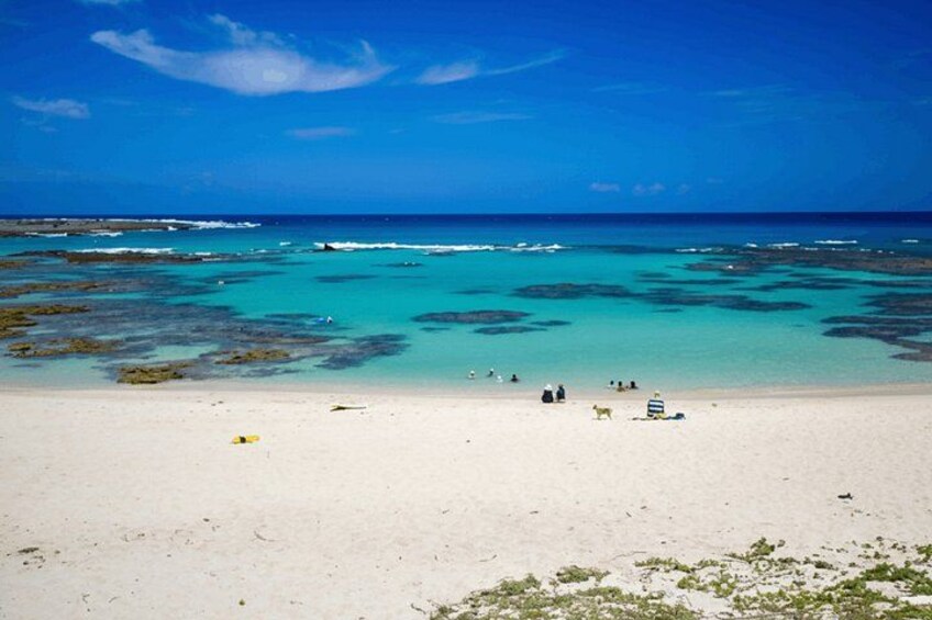 A beach with clear turquoise water, white sand, and sparse vegetation. 2