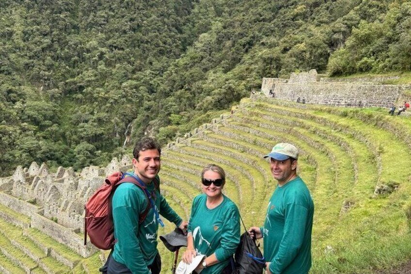 Tres personas de pie en una ladera escalonada con antiguas construcciones de piedra al fondo. 1