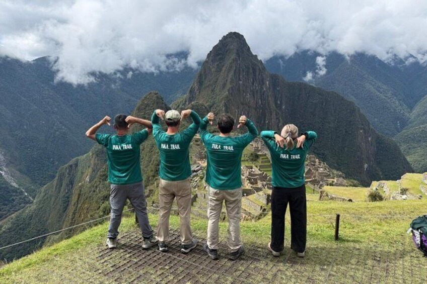 Cuatro personas con camisetas verdes que tienen la inscripción 'Pinta Trail' en la parte de atrás, de pie en una zona cubierta de césped con un paisaje montañoso al fondo. 3