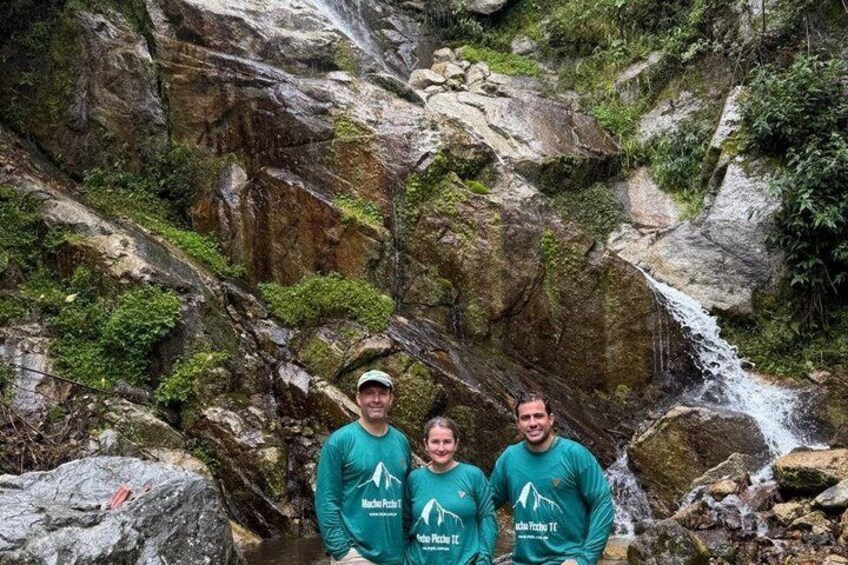Tres personas de pie frente a una cascada rocosa. 5