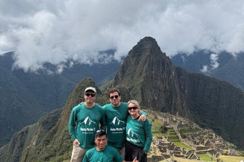 Un grupo de personas con camisetas verdes idénticas frente a Machu Picchu, con una montaña al fondo. 2
