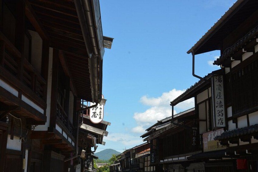 A narrow street with traditional Japanese buildings, a clear sky, and a mountain in the background. 2
