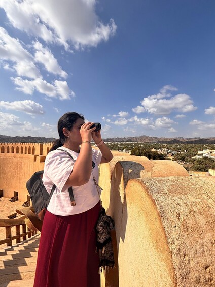 A person using binoculars overlooking a historic fort with a clear sky. 5