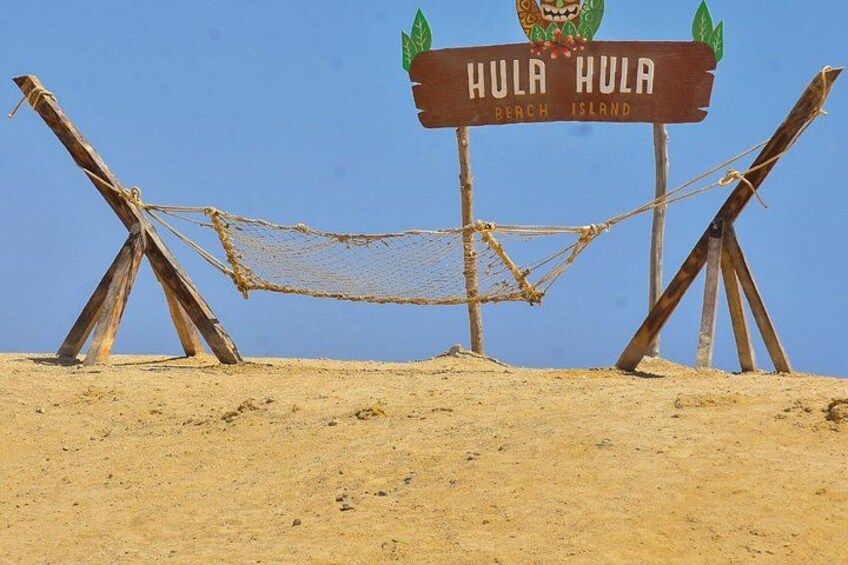 A beach sign with the text 'Hula Hula Beach Island' and a hammock strung between wooden poles. 5