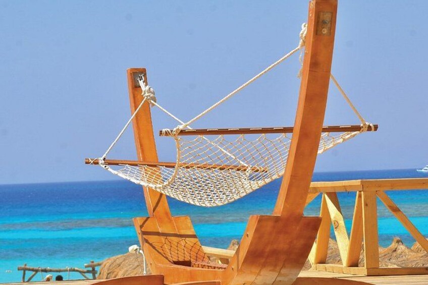 A wooden hammock suspended between two posts, overlooking a turquoise sea. 1