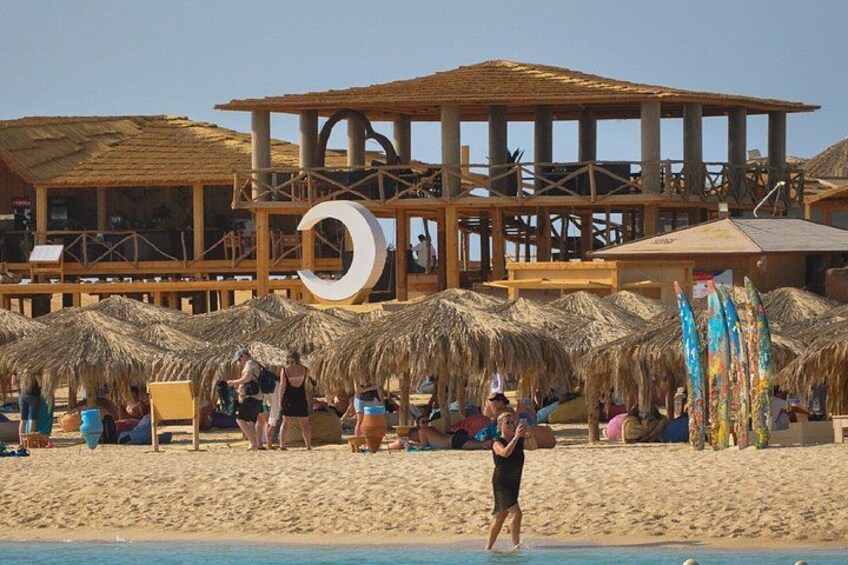 A beach with thatched umbrellas, wooden structures, and people relaxing. 2
