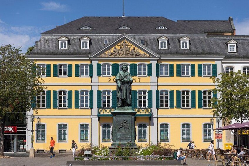 En gul bygning med grønne skodder, en statue og folk, der går forbi. 5