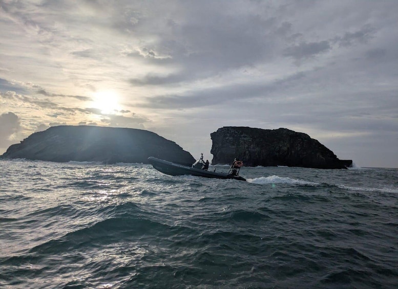 A boat navigating near rocky cliffs with the sun setting in the background. 3