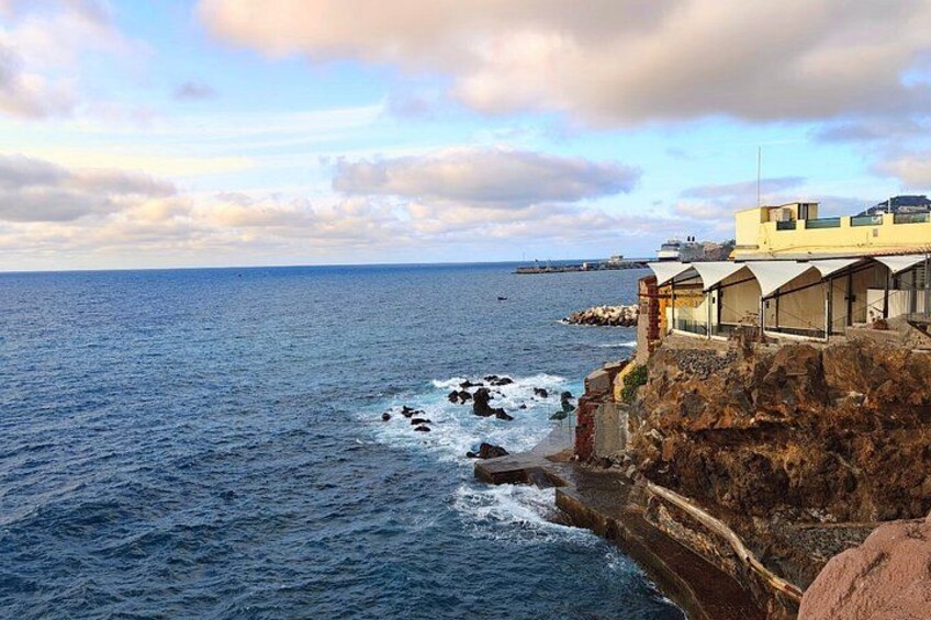 A coastal scene with a rocky cliff, a building with a flat roof, and the ocean. 3
