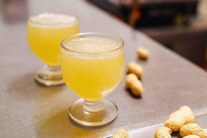 Two glasses of a yellow beverage on a bar counter with peanuts scattered around. 1