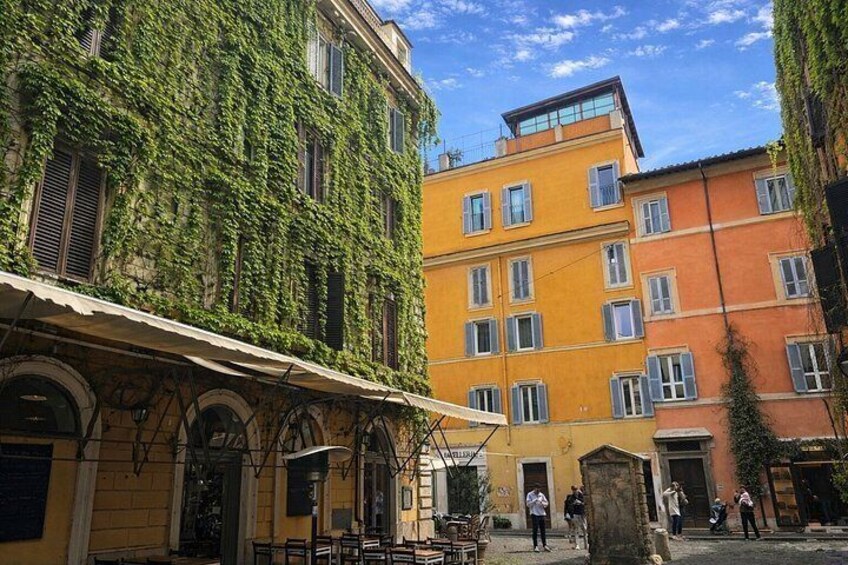 Ein Innenhof mit Efeu bewachsenen Gebäuden, ein Café mit Außenbestuhlung und einem strahlend blauen Himmel. 3