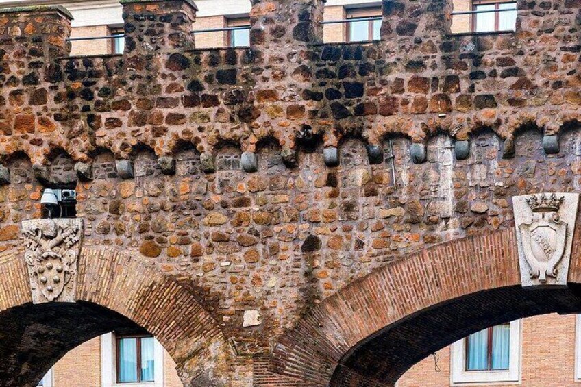Ein steinerer Bogen mit Wappen und einem Gebäude im Hintergrund. 4