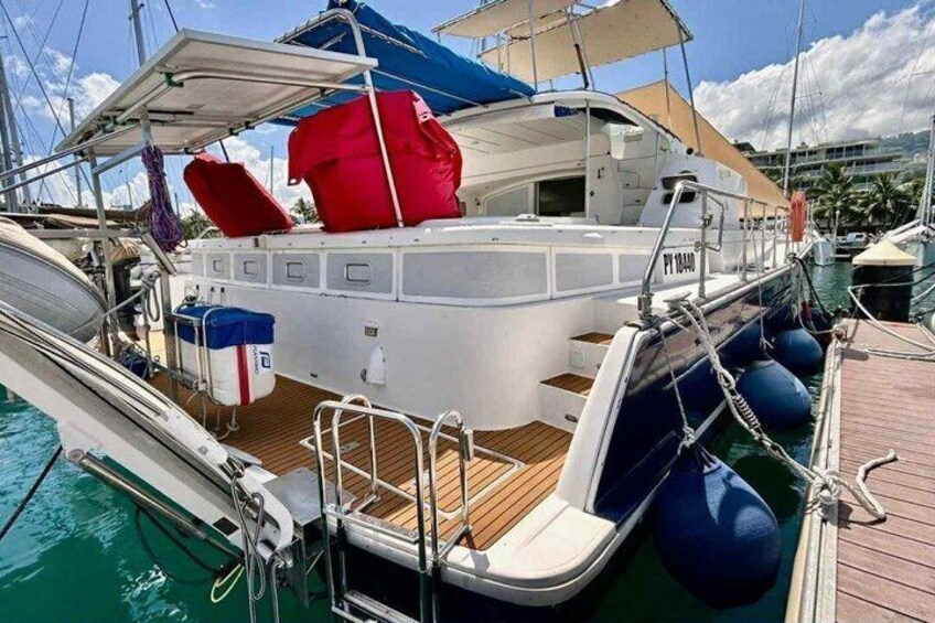 A white yacht docked at a marina with a wooden deck, life rings, and a red and blue canopy. 3