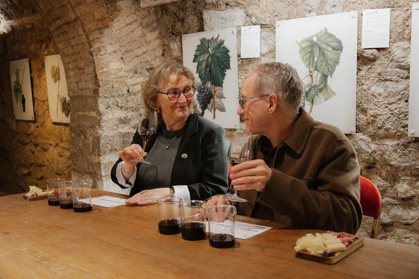 Two people sitting at a wooden table with wine glasses and a plate of food. 2