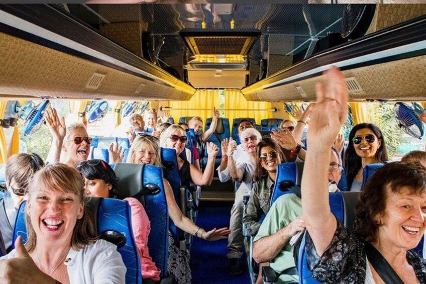 A group of people on a bus, some raising their hands, with blue seats and yellow interior. 2