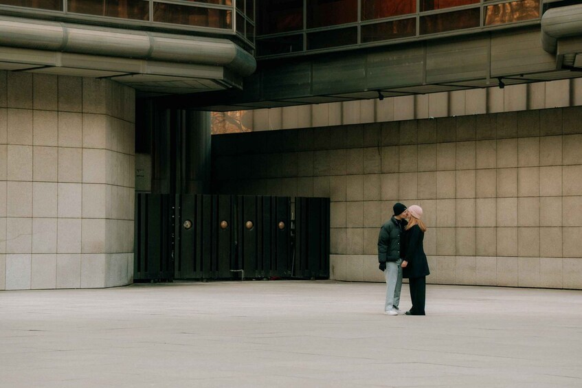 A man and woman standing in front of a building with a large black door and a tiled facade. 2