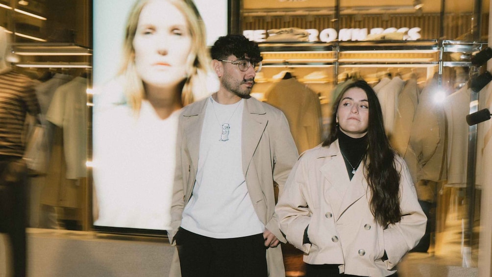 Two people standing in front of a clothing store with a large advertisement. 5