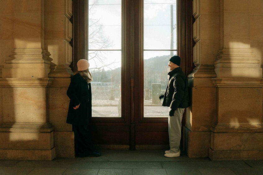 Two people standing in a doorway with large windows, looking outside. 3