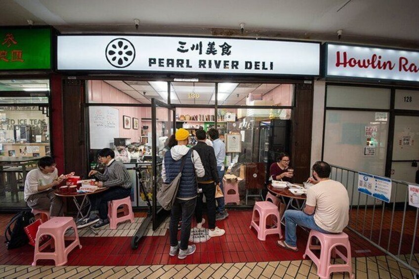 Un espace de restauration avec des personnes assises à des tables, une enseigne indiquant le nom de « Pearl River Deli » et une enseigne « Howlin Ra ». 2