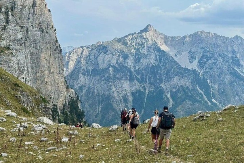 Hikers on a mountain trail with rocky cliffs and a mountain range in the background. 1