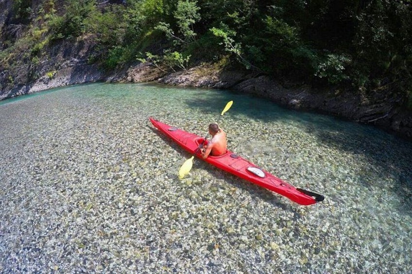 Une personne fait du kayak sur une rivière aux eaux claires, entourée d'un paysage rocheux et de verdure. 2