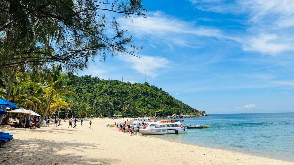 A beach with people, boats, and a forested hill. 2