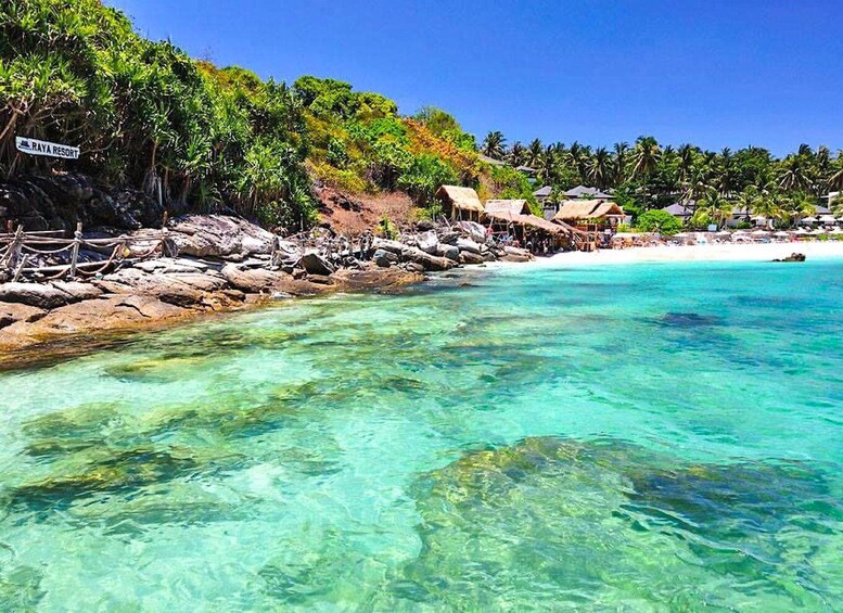 A clear turquoise sea, a rocky shoreline, and a resort named 'Raya Resort' with thatched-roof huts. 4