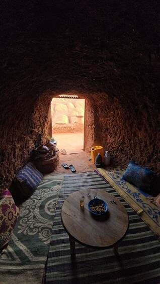 An interior of a cave with a stone table, cushions, and a bowl of snacks. 2