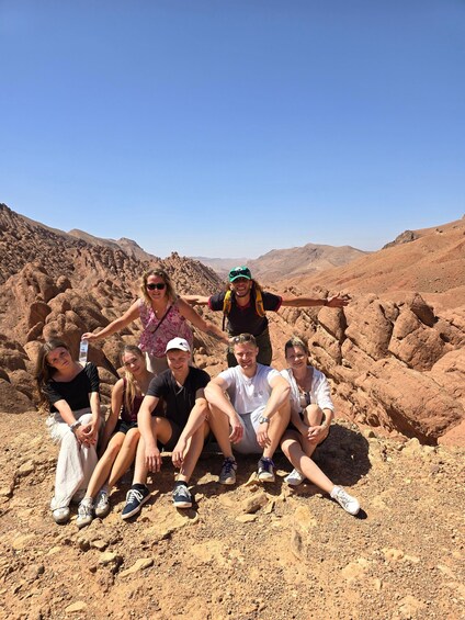A group of people sitting on a rocky terrain with a desert landscape in the background. 5
