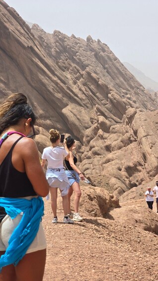 A group of people hiking on a rocky trail with a large, rugged mountain in the background. 1