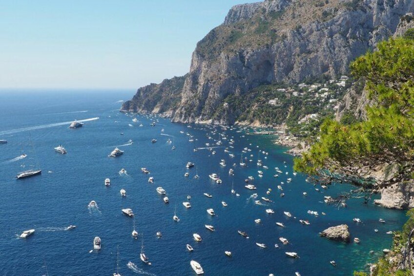 A coastal area with numerous boats anchored in the water, rocky cliffs, and sparse vegetation. 4