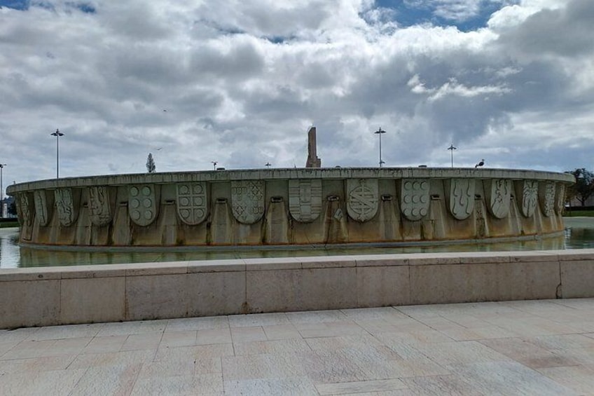 Una fuente circular con diseños intrincados y una estatua central, rodeada de un sendero adoquinado. 2