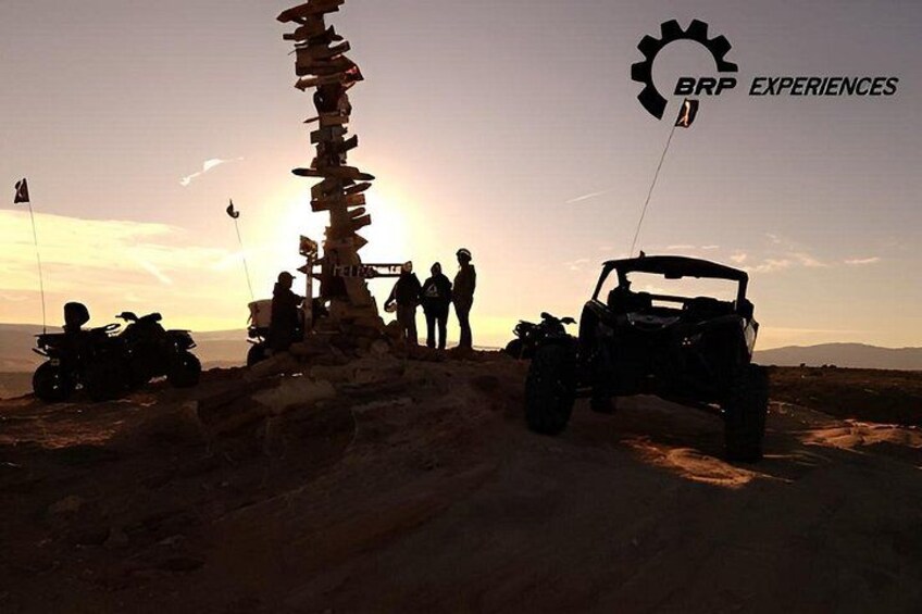 Paesaggio desertico con un cairn di pietra, veicoli fuoristrada e un tramonto. 1
