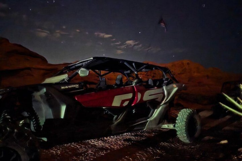 Un veicolo fuoristrada rosso e nero con il numero 25 sul fianco, parcheggiato su un terreno roccioso con un paesaggio desertico sullo sfondo. 3