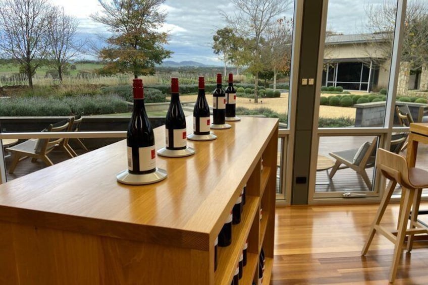 A wooden table with wine bottles and chairs in a room with a view of the outdoors. 1