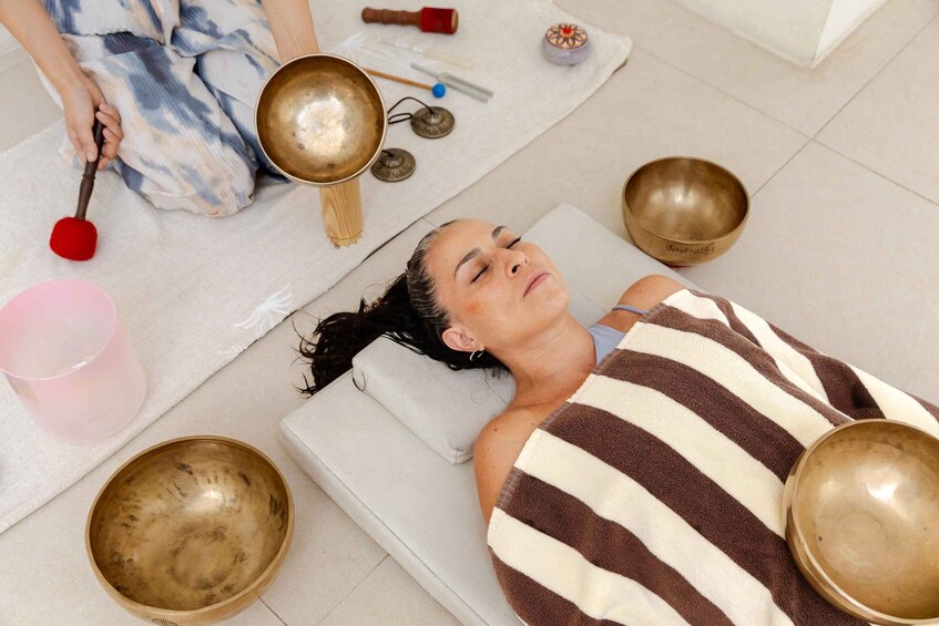 A person lying on a mat with multiple bowls and a red mallet. 5