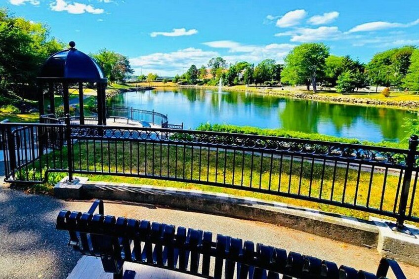 A park with a gazebo, a pond, and a metal fence. 2