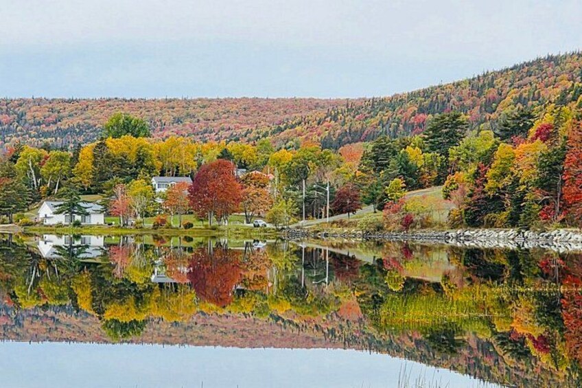 A lake reflecting colorful autumn trees, a house, and a forested hill. 4