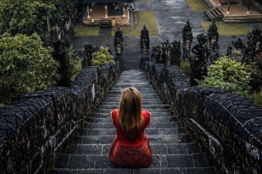 Une femme est assise sur des marches de pierre menant à un temple orné de statues. 3