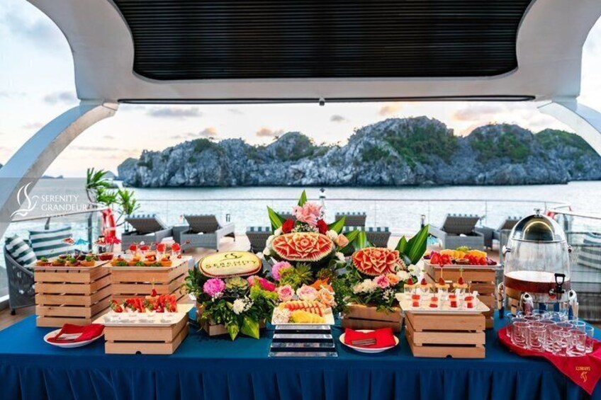 A buffet table on a boat with various food items and a backdrop of rocky cliffs. 3