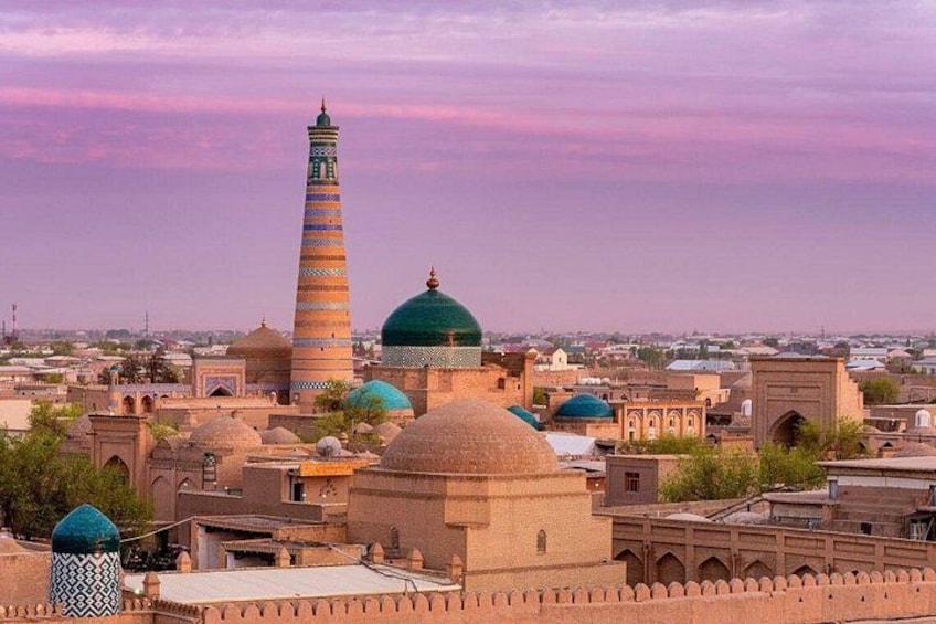 A historic cityscape with a prominent minaret, domed buildings, and a fortified wall. 1