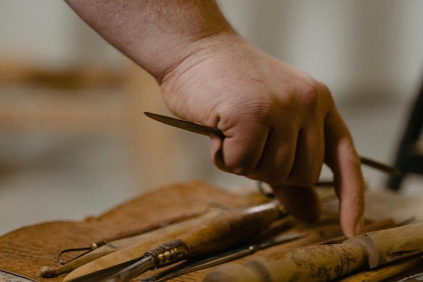 A hand holding a knife, working on a wooden surface with tools. 3