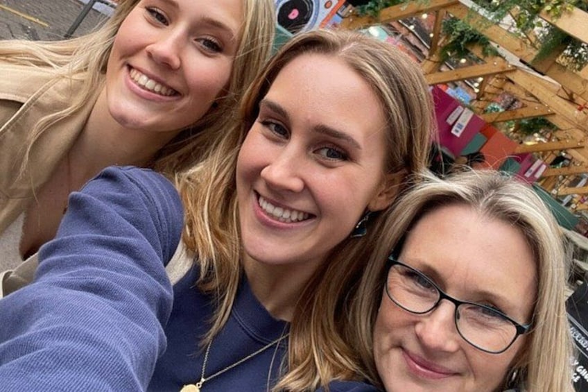Three people taking a selfie in an outdoor setting with a wooden structure and greenery in the background. 2