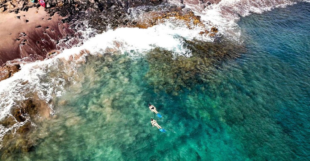 An aerial view of a beach with clear turquoise water and two people swimming. 4