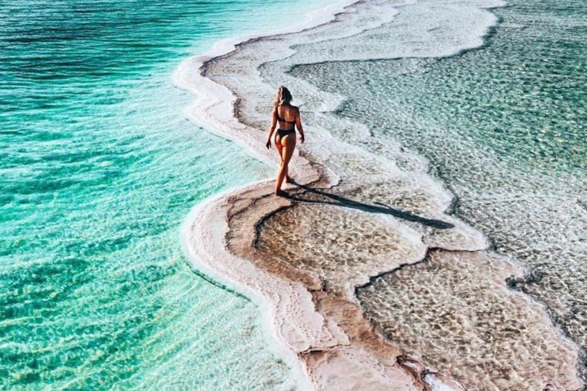A person standing on a beach with clear turquoise water and white sand. 2