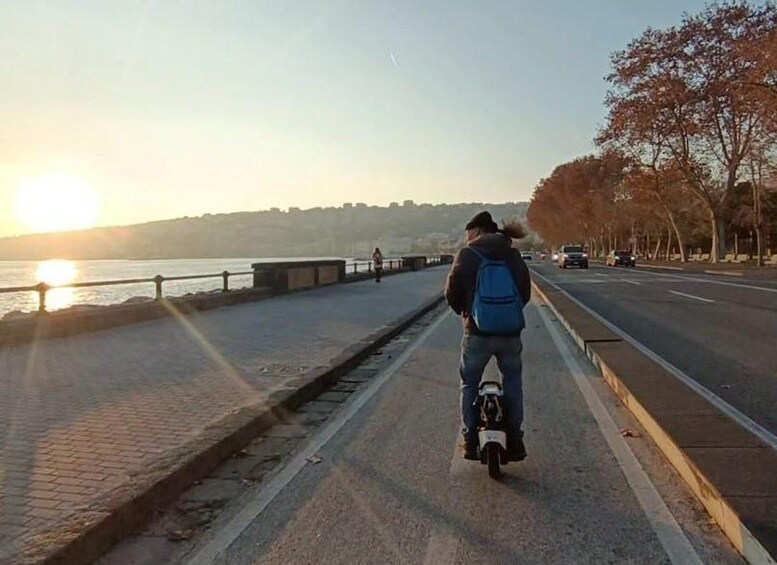 A person riding a unicycle on a paved path beside a road, with a sunset in the background. 3