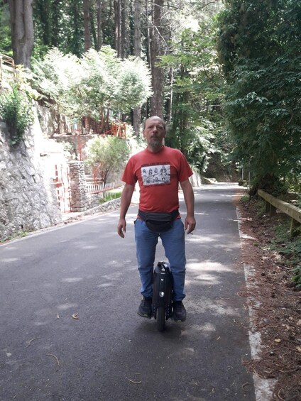 A man on a scooter on a paved road surrounded by trees and stone walls. 2