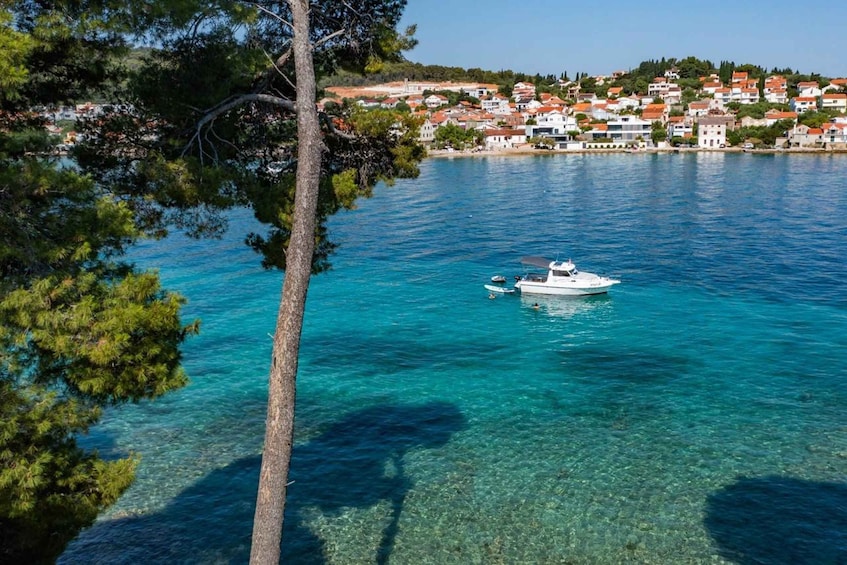 A clear blue sea with a boat, a tree, and a coastal town in the background. 2