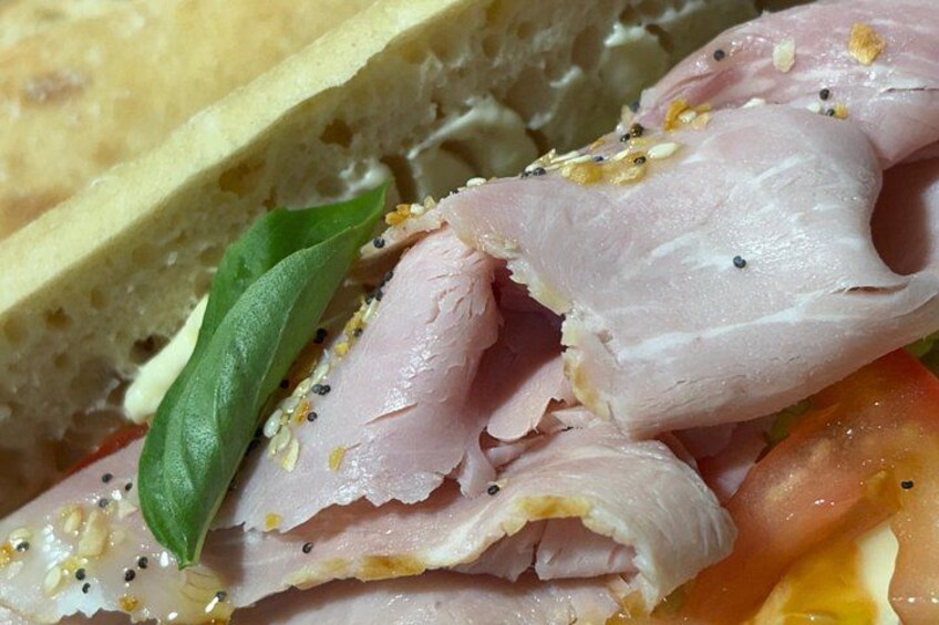 Ein Sandwich mit Fleischscheiben, einem Basilikumblatt und Sesamsamen. 3